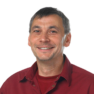 Ein lächelnder Mann in einem roten Hemd blickt freundlich in die Kamera.