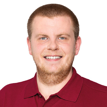 Ein lächelnder Auszubildender in einem roten Polohemd blickt direkt in die Kamera.