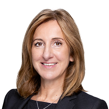 Eine Frau mit schulterlangem Haar lächelt freundlich in die Kamera und trägt einen dunklen Blazer.