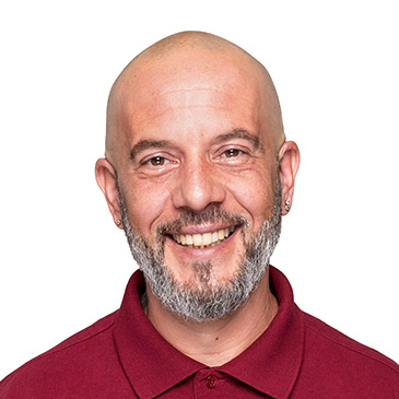 Ein lächelnder Mann im roten Polohemd steht vor einem weißen Hintergrund.