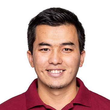 Ein junger Mann in einem roten Polohemd lächelt freundlich in die Kamera.