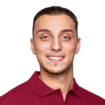 Ein junger Mann in einem roten Polohemd lächelt freundlich in die Kamera.