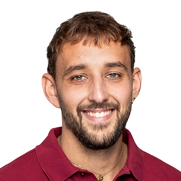 Ein lächelnder Mann in einem roten Hemd blickt direkt in die Kamera.