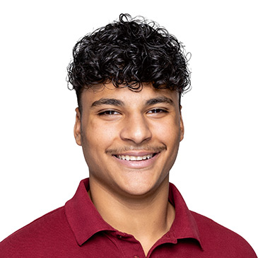 Ein junger Mann mit lockigem Haar lächelt freundlich in die Kamera, während er ein weinrotes Polohemd trägt.